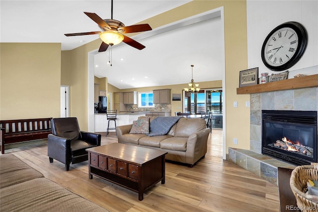 living area featuring a fireplace, vaulted ceiling, ceiling fan with notable chandelier, recessed lighting, and light wood-style flooring