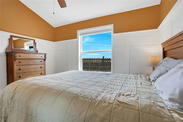 bedroom featuring ceiling fan, a wainscoted wall, lofted ceiling, and a decorative wall
