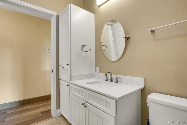 half bath featuring vanity, baseboards, wood finished floors, and toilet
