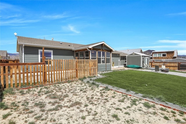 rear view of property featuring an outdoor structure, fence, a sunroom, a storage shed, and a yard