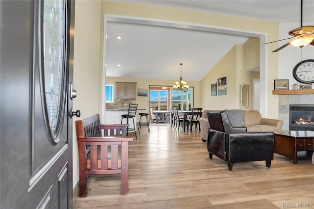 living area featuring light wood-style floors, high vaulted ceiling, a fireplace, and ceiling fan with notable chandelier