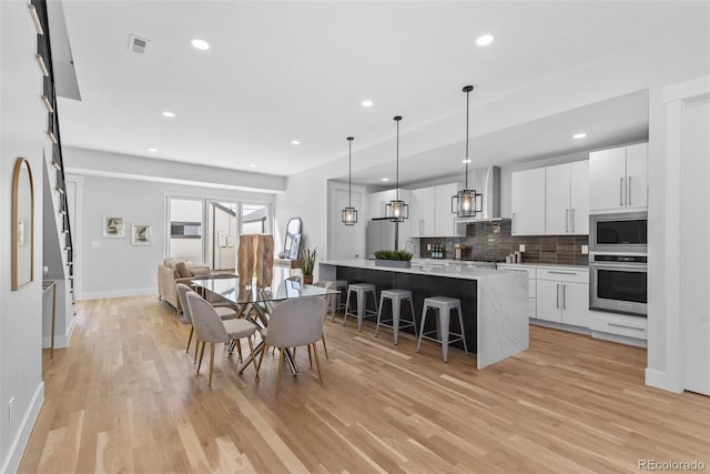 kitchen with appliances with stainless steel finishes, white cabinetry, a kitchen breakfast bar, a center island, and wall chimney range hood