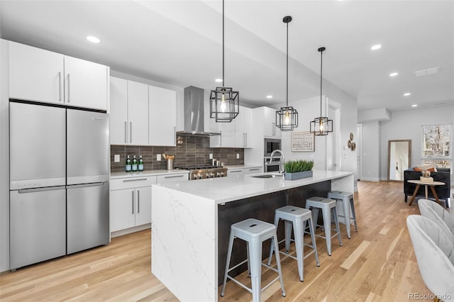 kitchen featuring an island with sink, appliances with stainless steel finishes, white cabinets, and wall chimney exhaust hood