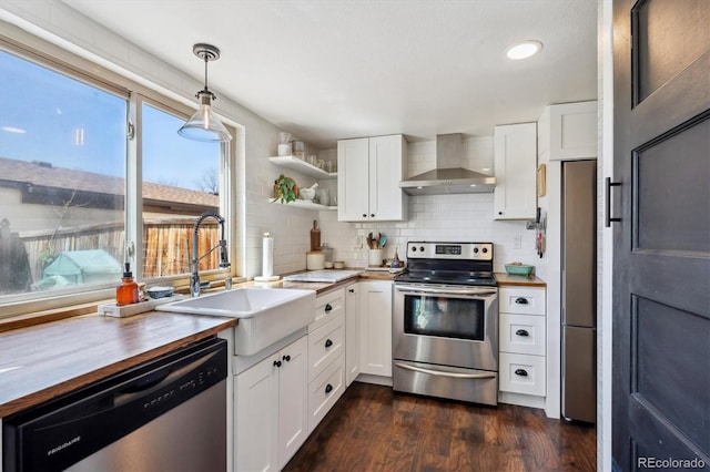 kitchen with dark wood-style flooring, butcher block counters, a sink, wall chimney range hood, and stainless steel appliances