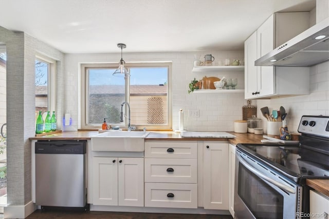 kitchen featuring butcher block counters, open shelves, wall chimney exhaust hood, stainless steel appliances, and white cabinets