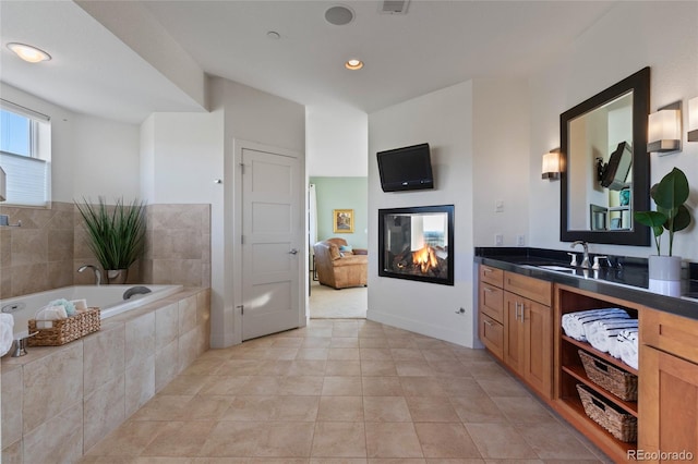 bathroom with tile patterned floors, tiled tub, vanity, and a multi sided fireplace