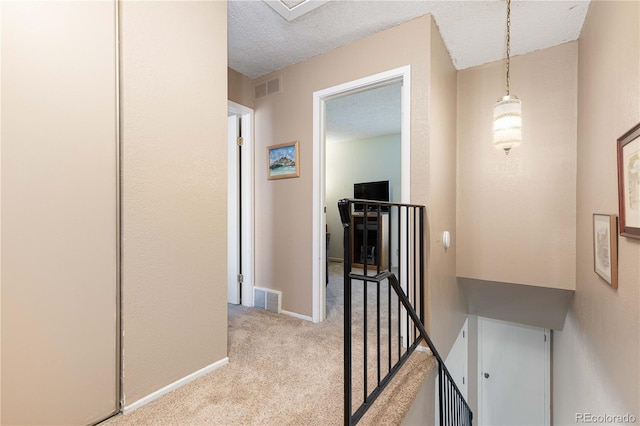 hall with light colored carpet and a textured ceiling