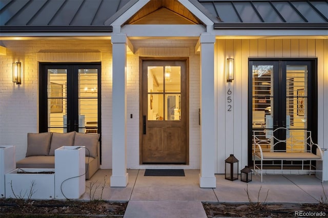 doorway to property with french doors, a standing seam roof, brick siding, metal roof, and a porch