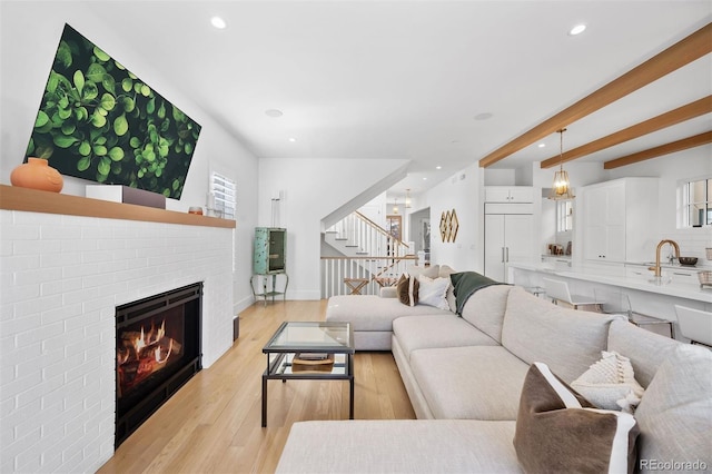 living room featuring stairway, a fireplace, recessed lighting, light wood-style flooring, and beamed ceiling