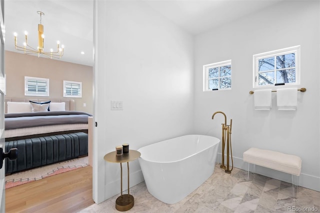 ensuite bathroom featuring a chandelier, a freestanding bath, and baseboards