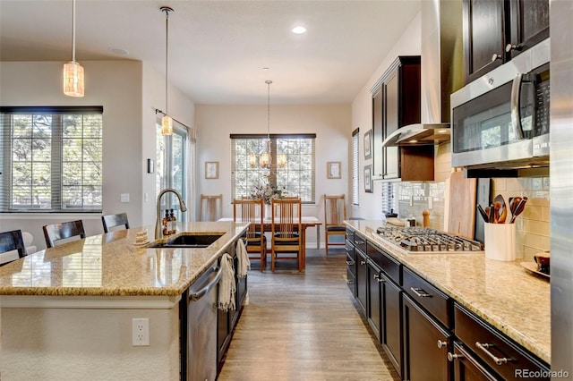 kitchen featuring decorative light fixtures, light stone counters, a kitchen island with sink, and appliances with stainless steel finishes