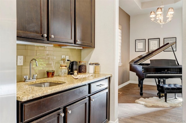 kitchen with sink, hanging light fixtures, light stone counters, light hardwood / wood-style floors, and dark brown cabinets