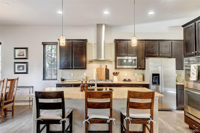 kitchen featuring a kitchen breakfast bar, wall chimney range hood, stainless steel appliances, and hanging light fixtures