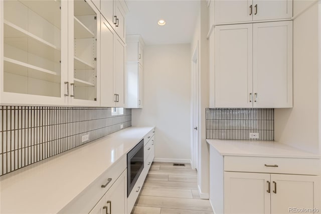 kitchen featuring light hardwood / wood-style floors, white cabinetry, stainless steel microwave, and tasteful backsplash