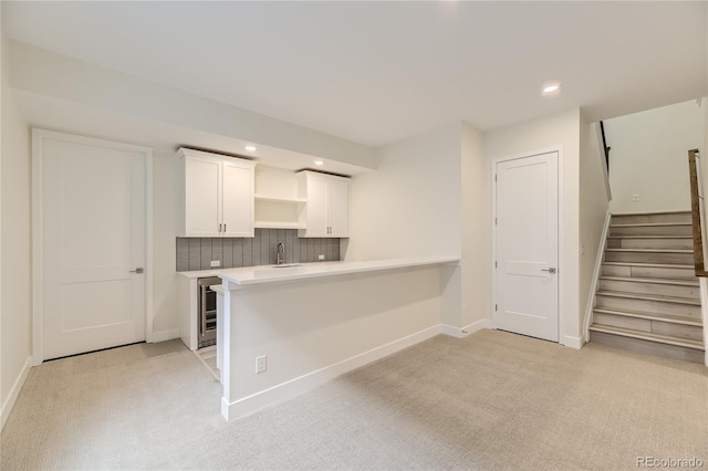 kitchen featuring tasteful backsplash, white cabinetry, light carpet, kitchen peninsula, and beverage cooler