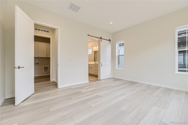 unfurnished bedroom featuring connected bathroom, a barn door, and light hardwood / wood-style flooring