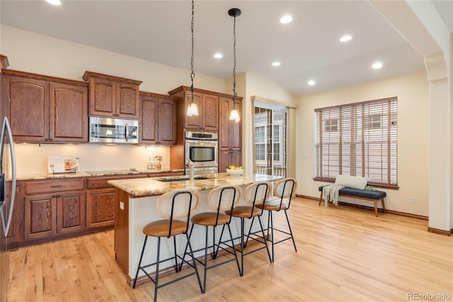 5723 S Union Ct, Littleton, CO 80127 - kitchen with appliances with stainless steel finishes, a kitchen island with sink, light wood-style flooring, light stone counters, and a breakfast bar