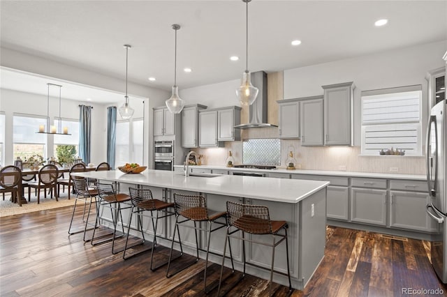 kitchen featuring a sink, gray cabinets, wall chimney exhaust hood, and a kitchen bar