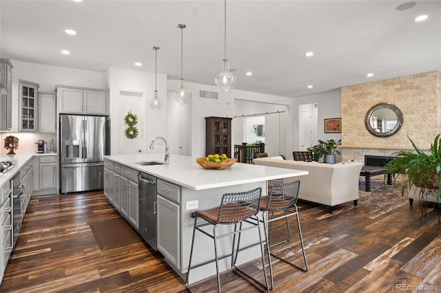 kitchen with a center island with sink, gray cabinetry, a sink, light countertops, and stainless steel appliances