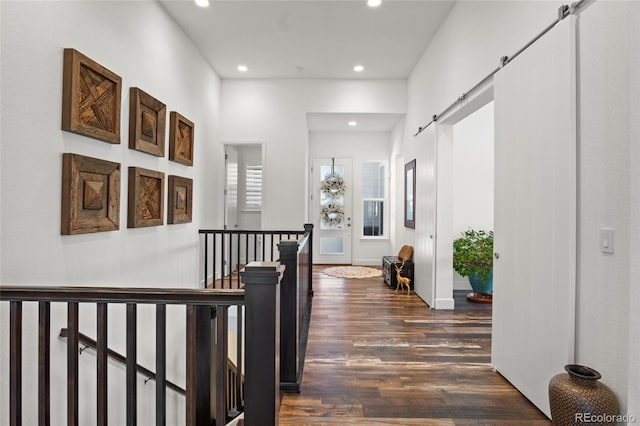 hallway with dark wood finished floors, a barn door, baseboards, an upstairs landing, and recessed lighting