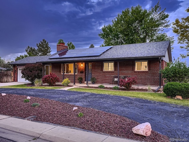 7112 S Platte Canyon Dr, Littleton, CO 80128 - ranch-style house with covered porch, an attached garage, a chimney, solar panels, and brick siding