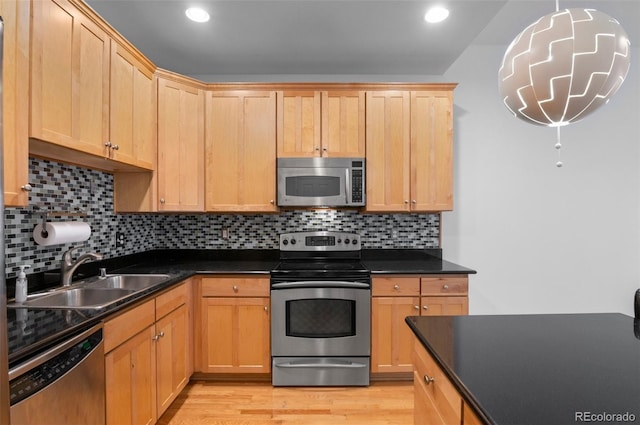 kitchen with a sink, dark countertops, light wood-type flooring, and stainless steel appliances