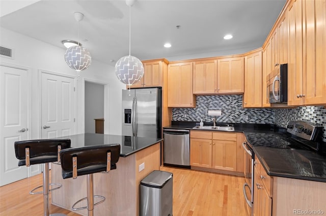 kitchen with a breakfast bar, light brown cabinets, light wood finished floors, and stainless steel appliances