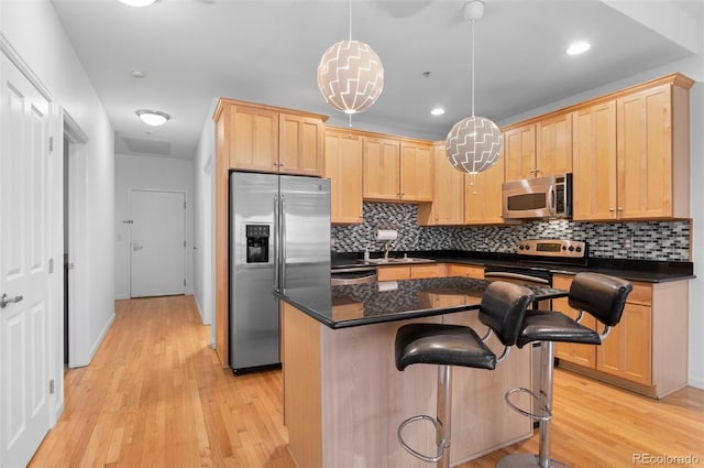 kitchen with dark countertops, light brown cabinetry, light wood-type flooring, appliances with stainless steel finishes, and a sink