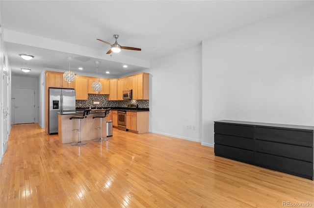 kitchen featuring an island with sink, appliances with stainless steel finishes, a kitchen bar, dark countertops, and tasteful backsplash