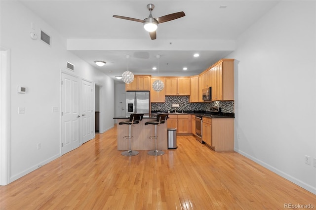 kitchen featuring visible vents, stainless steel appliances, decorative backsplash, dark countertops, and a kitchen breakfast bar