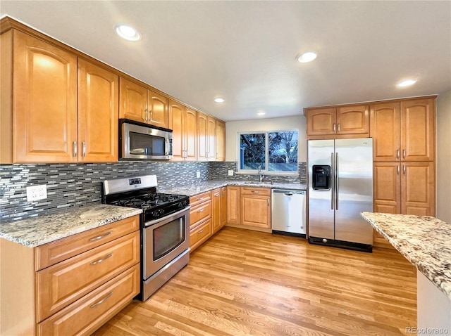 kitchen with light stone countertops, light wood-type flooring, stainless steel appliances, and sink