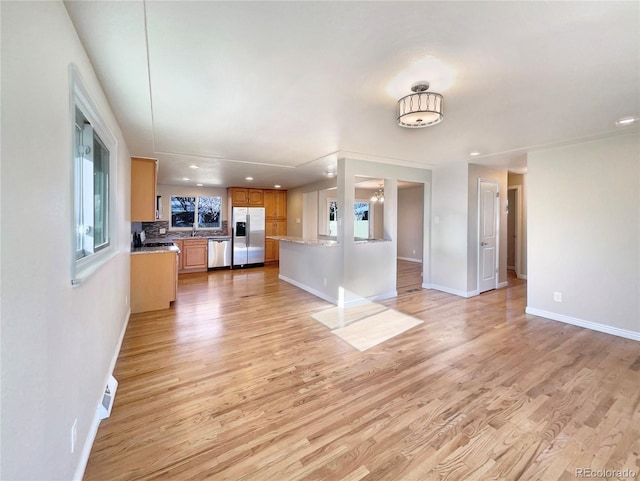 unfurnished living room featuring sink, a healthy amount of sunlight, and light wood-type flooring