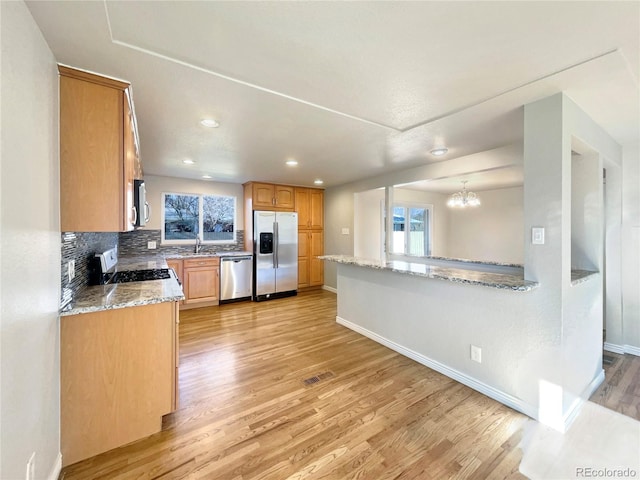 kitchen featuring sink, light stone counters, light hardwood / wood-style flooring, decorative backsplash, and appliances with stainless steel finishes