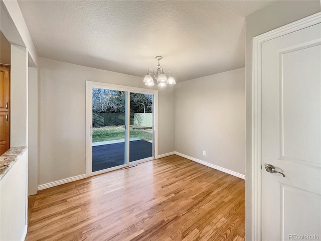 unfurnished dining area with a textured ceiling, light hardwood / wood-style floors, and a notable chandelier