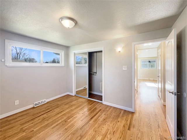 unfurnished bedroom with light wood-type flooring, a textured ceiling, and a closet