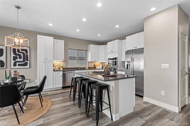 kitchen with appliances with stainless steel finishes, hardwood / wood-style floors, white cabinetry, a breakfast bar area, and a center island