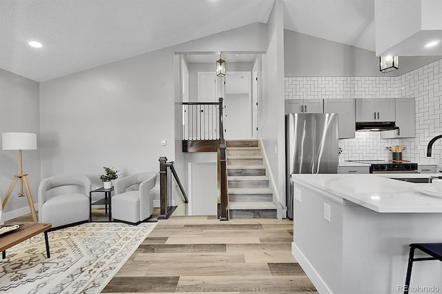 kitchen with lofted ceiling, sink, stainless steel refrigerator, gray cabinetry, and a kitchen breakfast bar