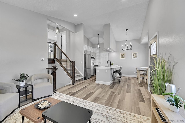 living room with sink, a chandelier, high vaulted ceiling, a textured ceiling, and light wood-type flooring