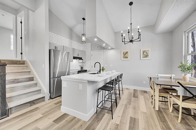 kitchen featuring decorative light fixtures, vaulted ceiling, stainless steel refrigerator, and a center island with sink