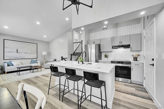 kitchen featuring a breakfast bar area, gray cabinetry, appliances with stainless steel finishes, a kitchen island with sink, and light hardwood / wood-style floors