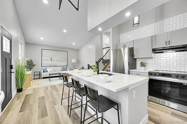 kitchen featuring a kitchen bar, sink, a center island with sink, gray cabinets, and stainless steel appliances