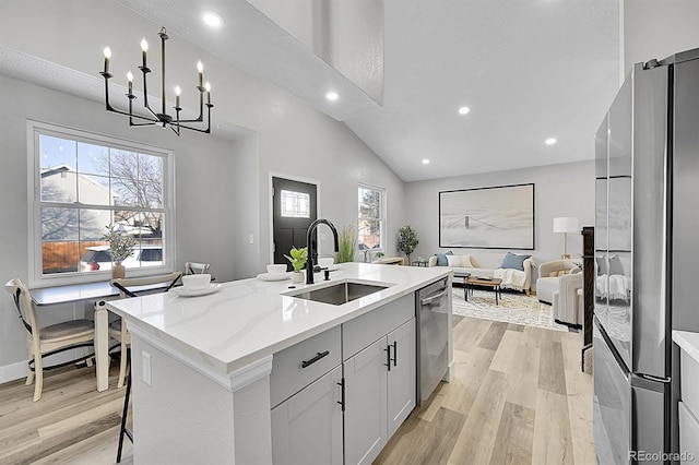 kitchen with sink, a kitchen island with sink, stainless steel appliances, light stone countertops, and light wood-type flooring