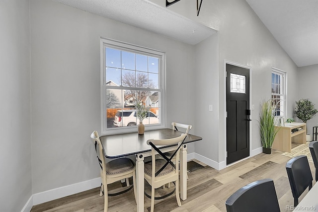 dining room featuring vaulted ceiling, a textured ceiling, and light wood-type flooring