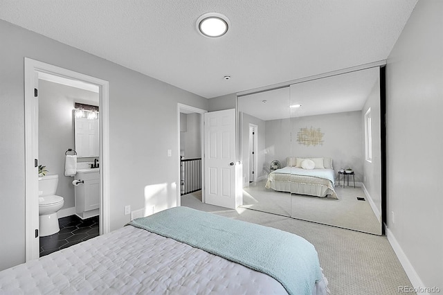 carpeted bedroom featuring sink, a textured ceiling, ensuite bath, and a closet