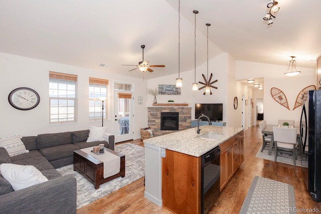 kitchen with black appliances, sink, light wood-type flooring, vaulted ceiling, and a kitchen island with sink