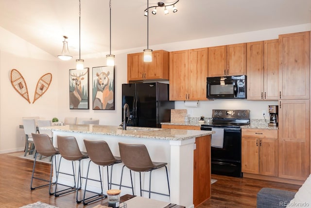 kitchen featuring light stone countertops, black appliances, a center island with sink, and dark hardwood / wood-style flooring