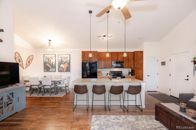 kitchen featuring a breakfast bar area, an island with sink, black appliances, decorative light fixtures, and dark hardwood / wood-style flooring