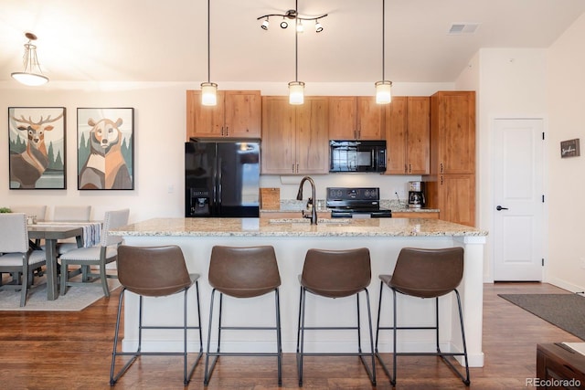 kitchen with dark wood-type flooring, black appliances, decorative light fixtures, and a kitchen island with sink