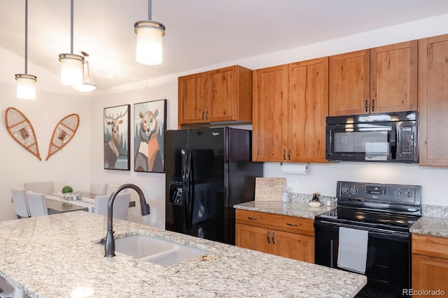 kitchen featuring black appliances, sink, hanging light fixtures, light stone counters, and a center island with sink