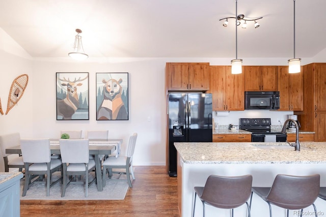 kitchen with hanging light fixtures, dark hardwood / wood-style flooring, light stone countertops, black appliances, and sink